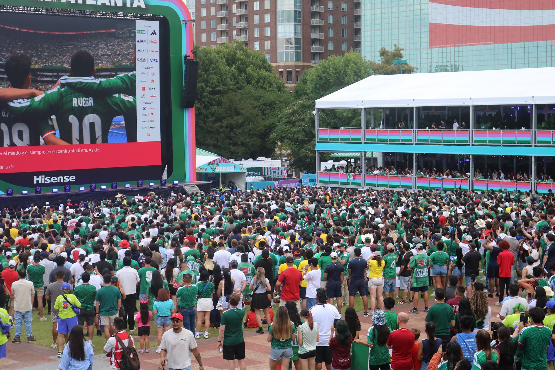 Crowd gathered in a park before a giant outdoor screen showing a sports event