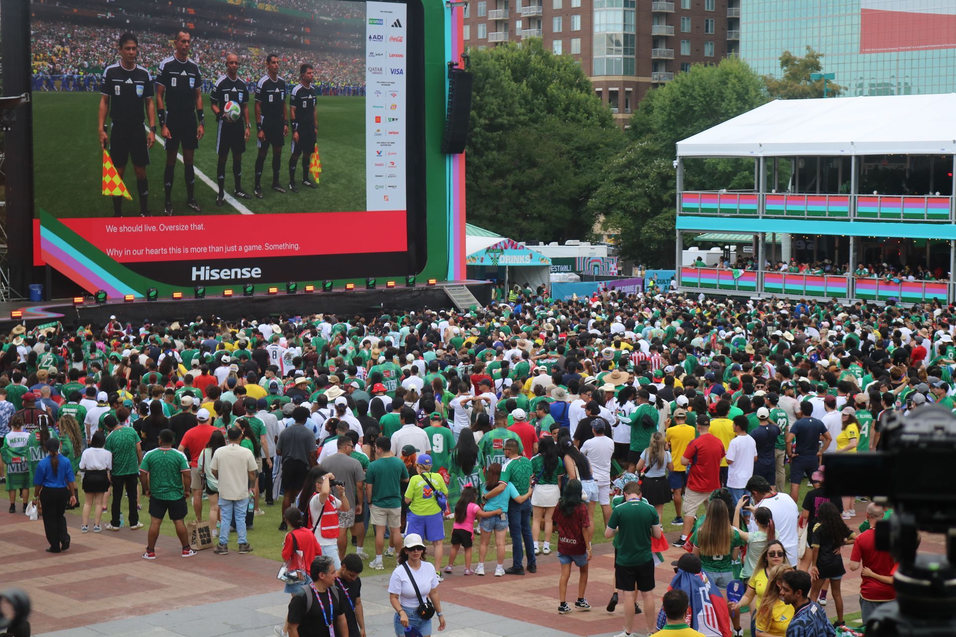 Crowd gathered outdoors watching a large screen showing a soccer team ceremony