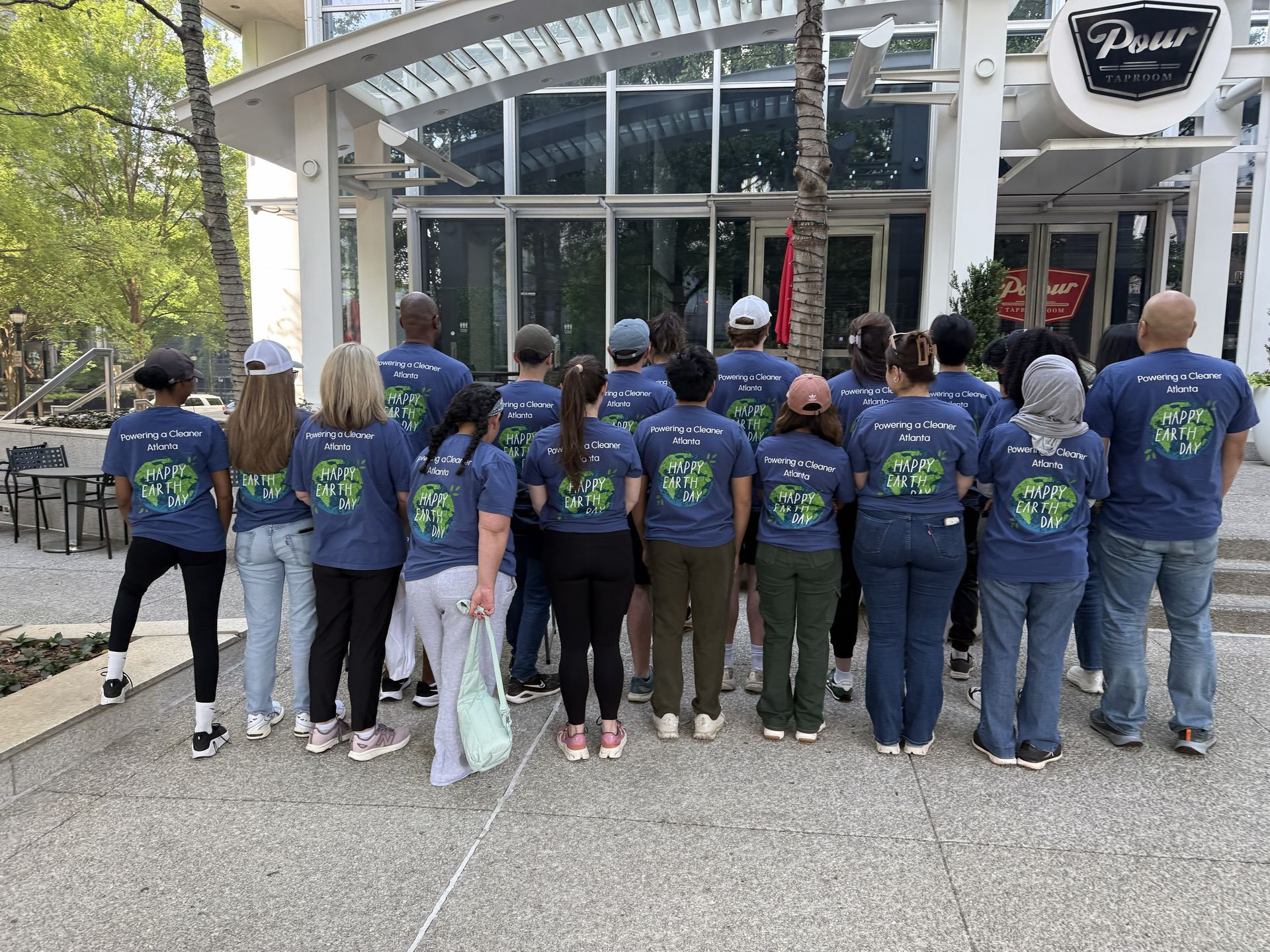 Group of people in matching blue shirts standing outside a glass storefront, seen from behind