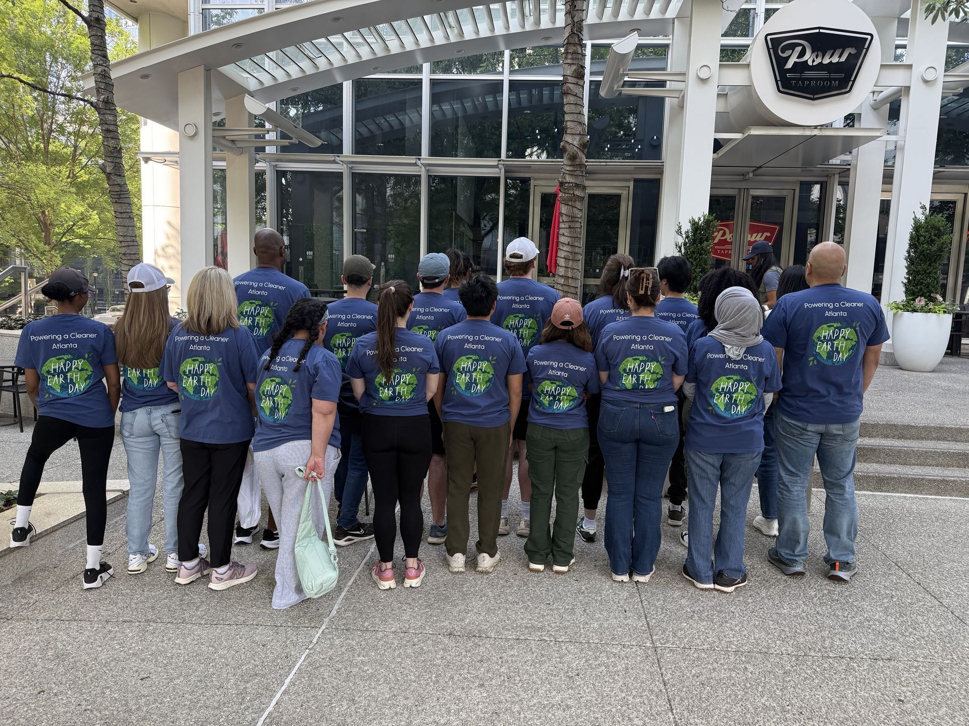 Group in matching blue shirts standing outside a building with a round sign and glass entrance