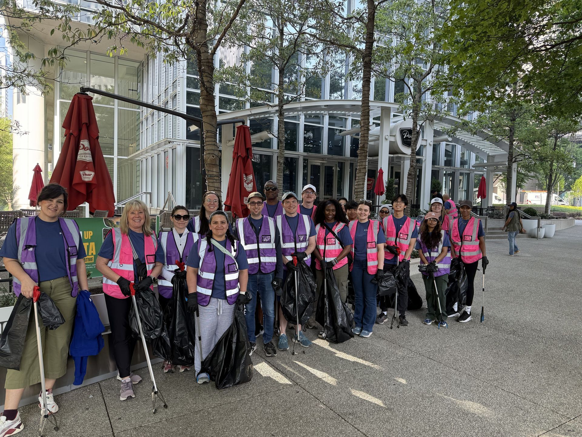 Group of hikers in pink safety vests holding trekking poles outdoors by a glass building