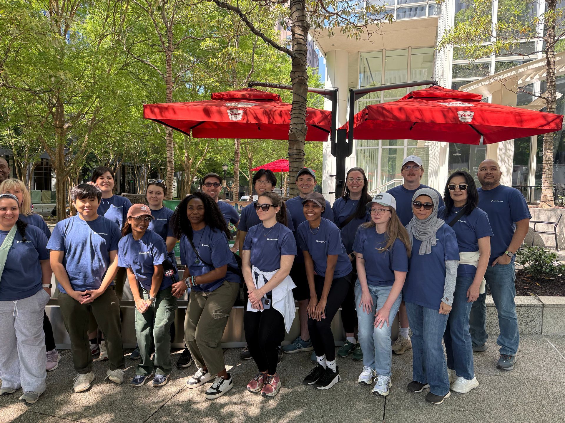 Group of people in blue shirts posing outdoors under red umbrellas in a park-like setting