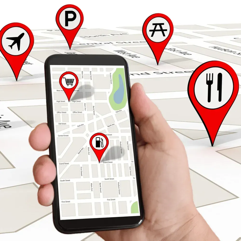 Hand holding smartphone displaying a map with location markers for airplane, parking, picnic, shopping cart, gas station, and restaurant.