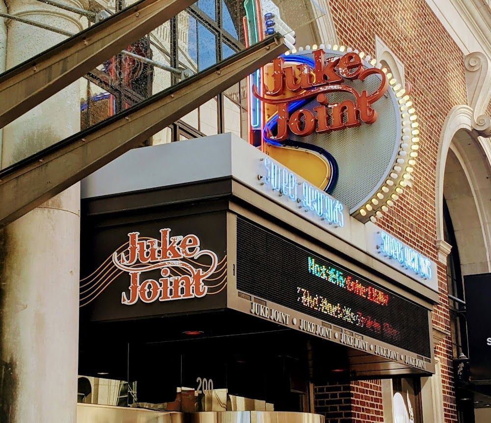Sign for Juke Joint, a restaurant. The sign has neon lights and an LED display showing upcoming shows.