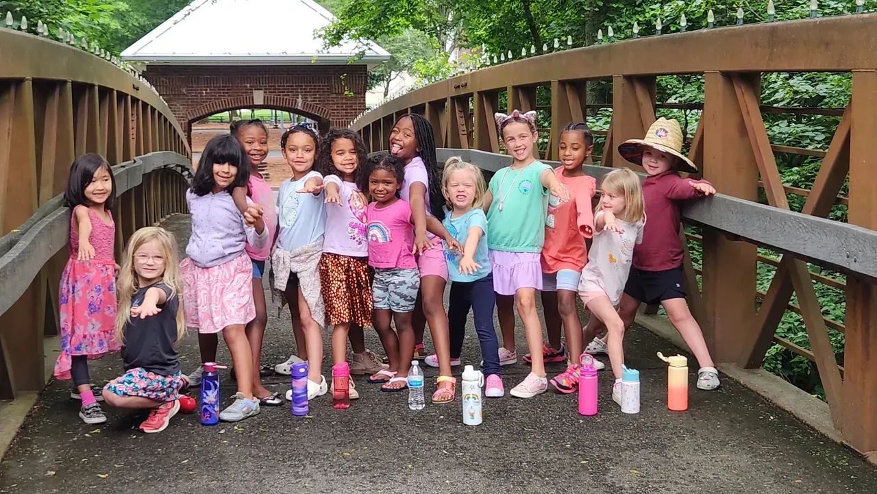 Group of children on a wooden bridge, smiling and posing with water bottles.