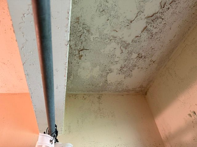 Corner of a ceiling and wall with water damage and mold discoloration near a pipe or beam