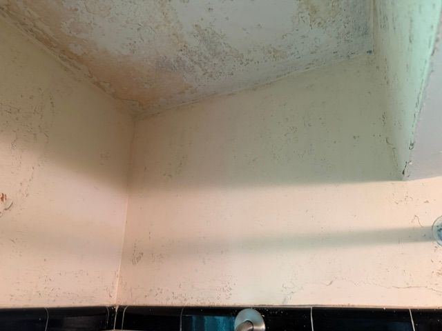 Dirty corner of a wall and ceiling with water stains and mold, above a tiled room with a sink edge below