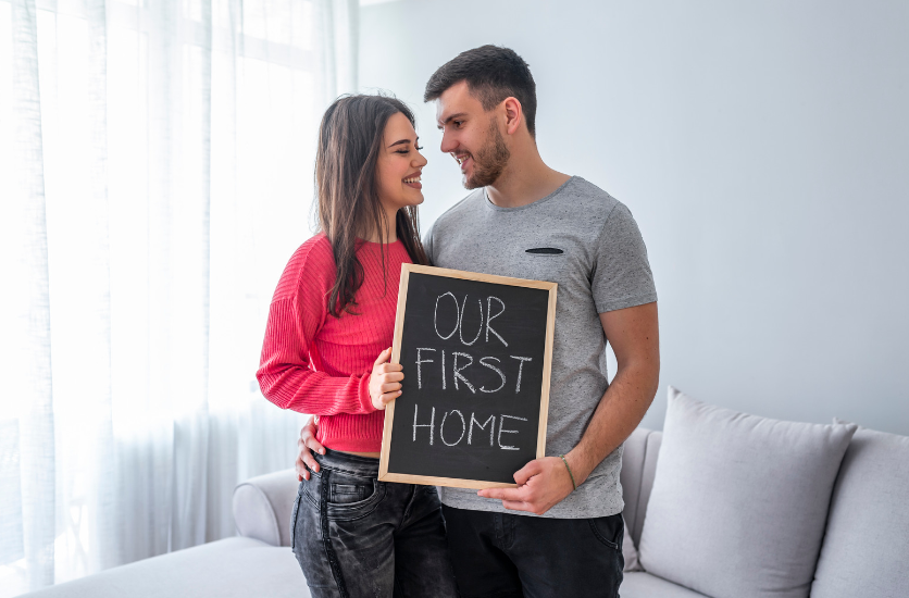 A man and a woman are holding a sign that says `` our first home ''.