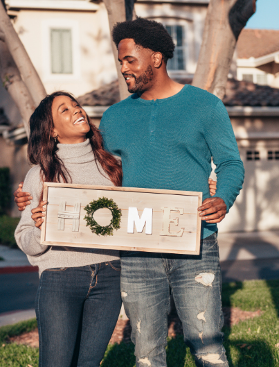 A man and a woman are holding a sign that says home.