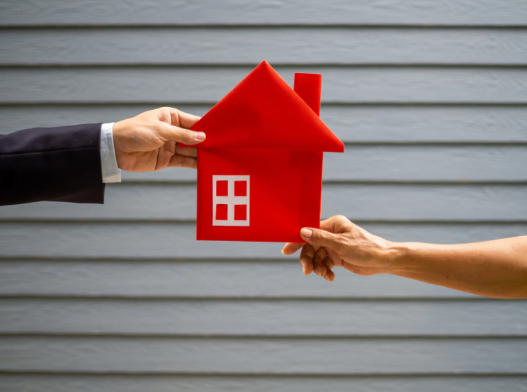A person is handing a red house to another person.