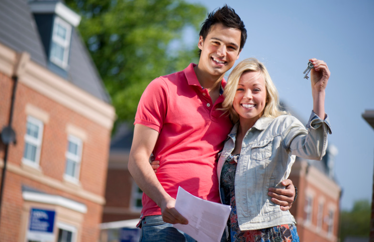 A man and a woman are standing in front of a house holding keys.