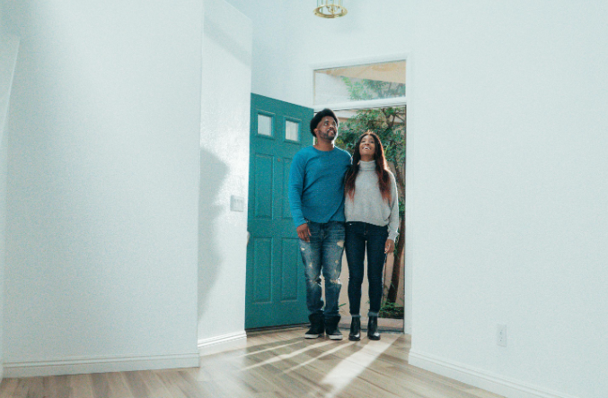 A man and a woman are standing in an empty room in front of a blue door.