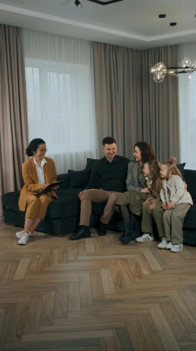 A family is sitting on a couch in a living room talking to a woman.