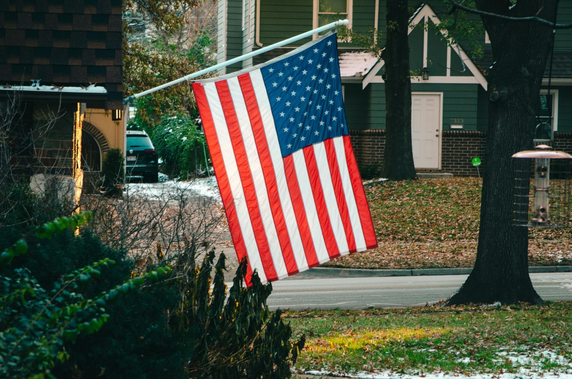 An american flag is hanging from a pole in front of a house.