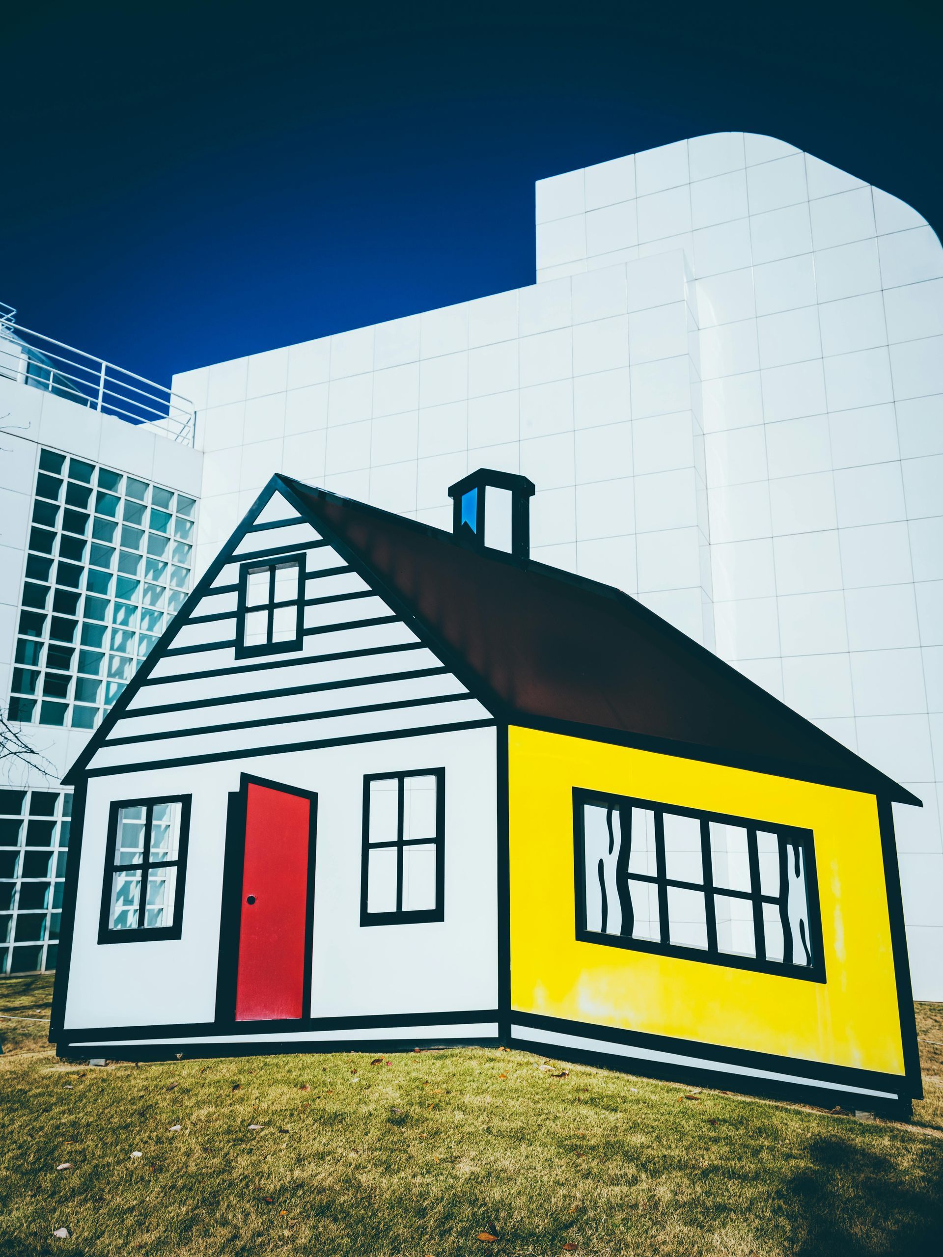 A yellow and white house with a red door in front of a white building