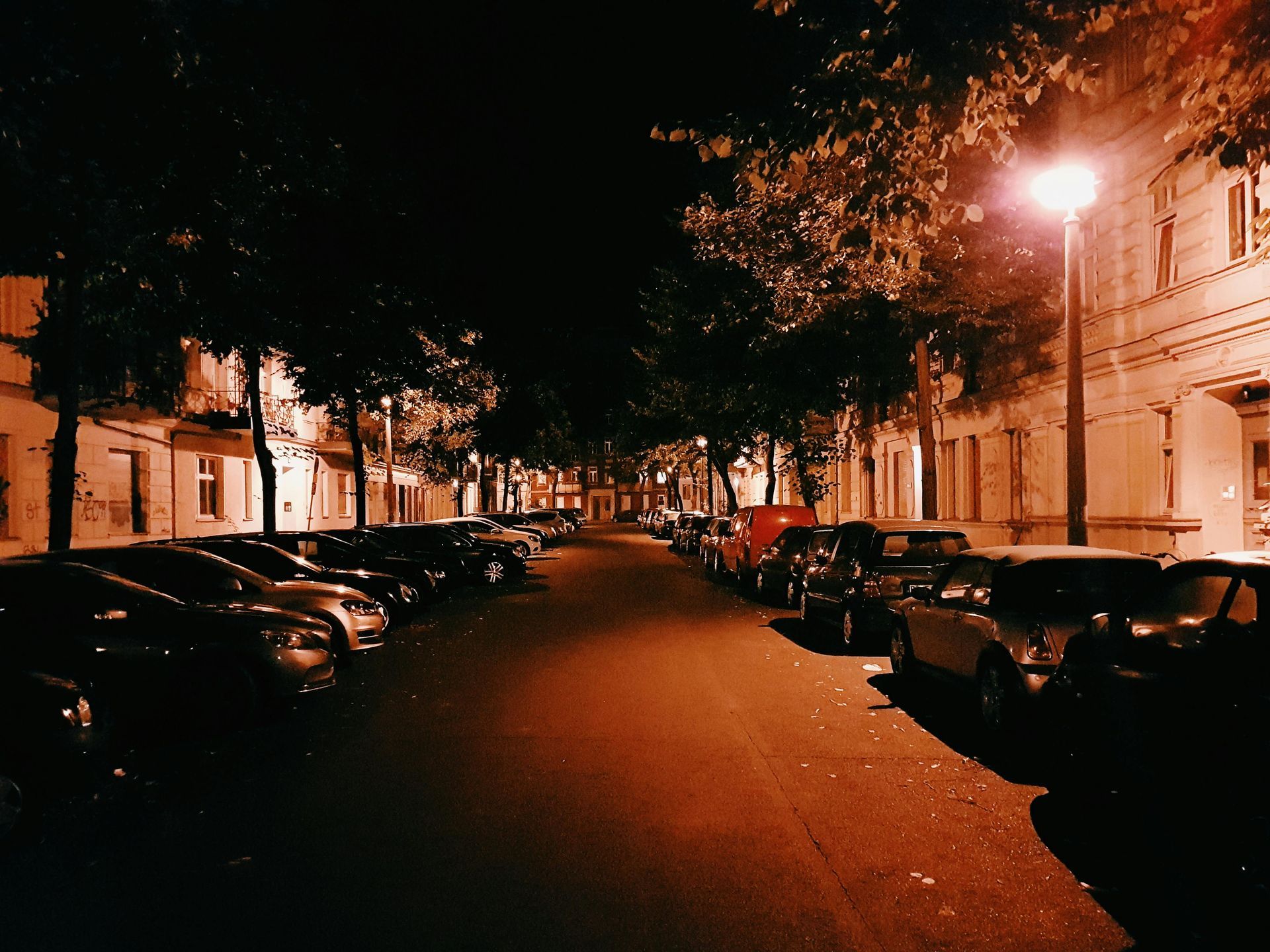A row of cars are parked on the side of a street at night