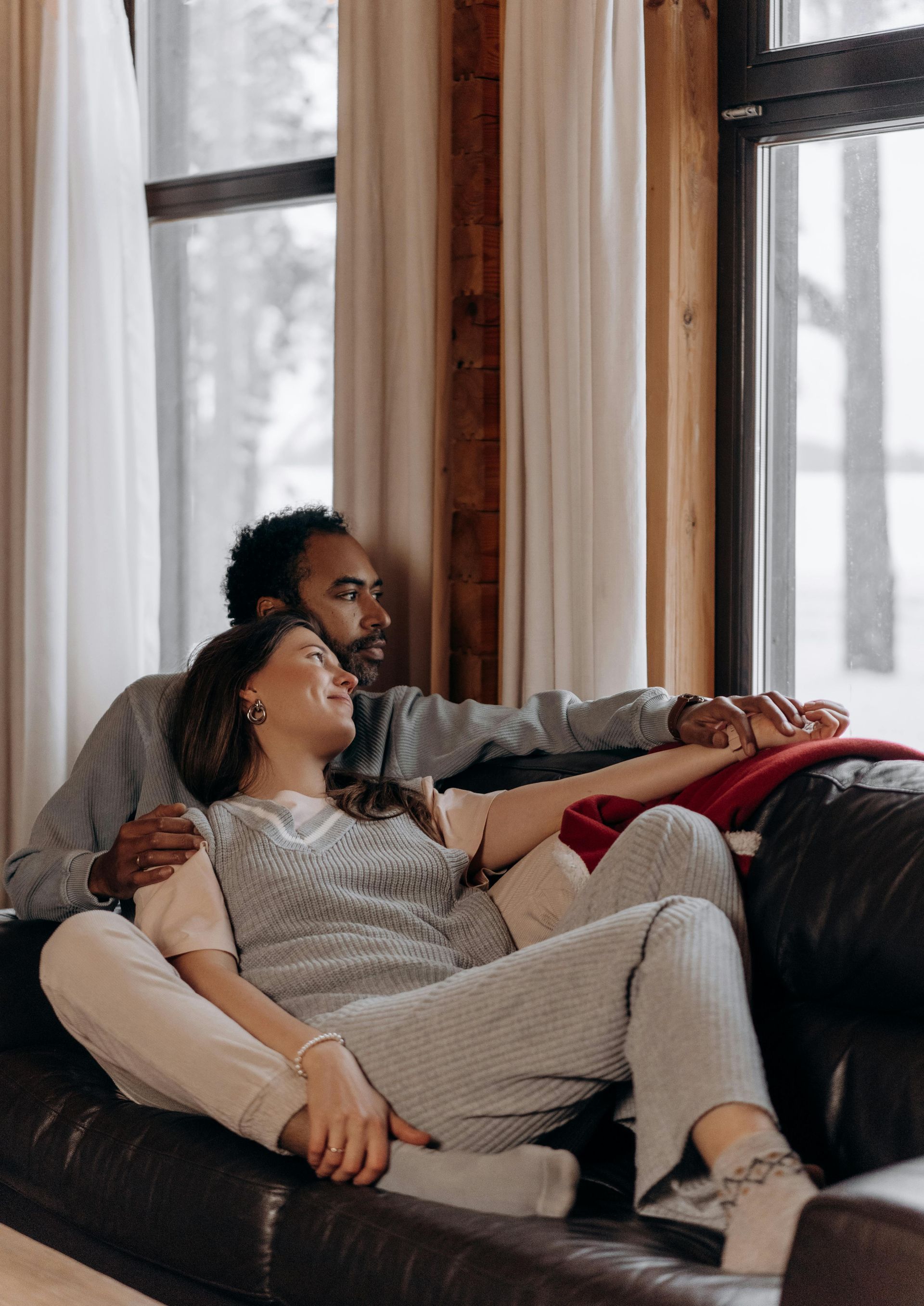 A man and a woman are sitting on a couch in front of a window.
