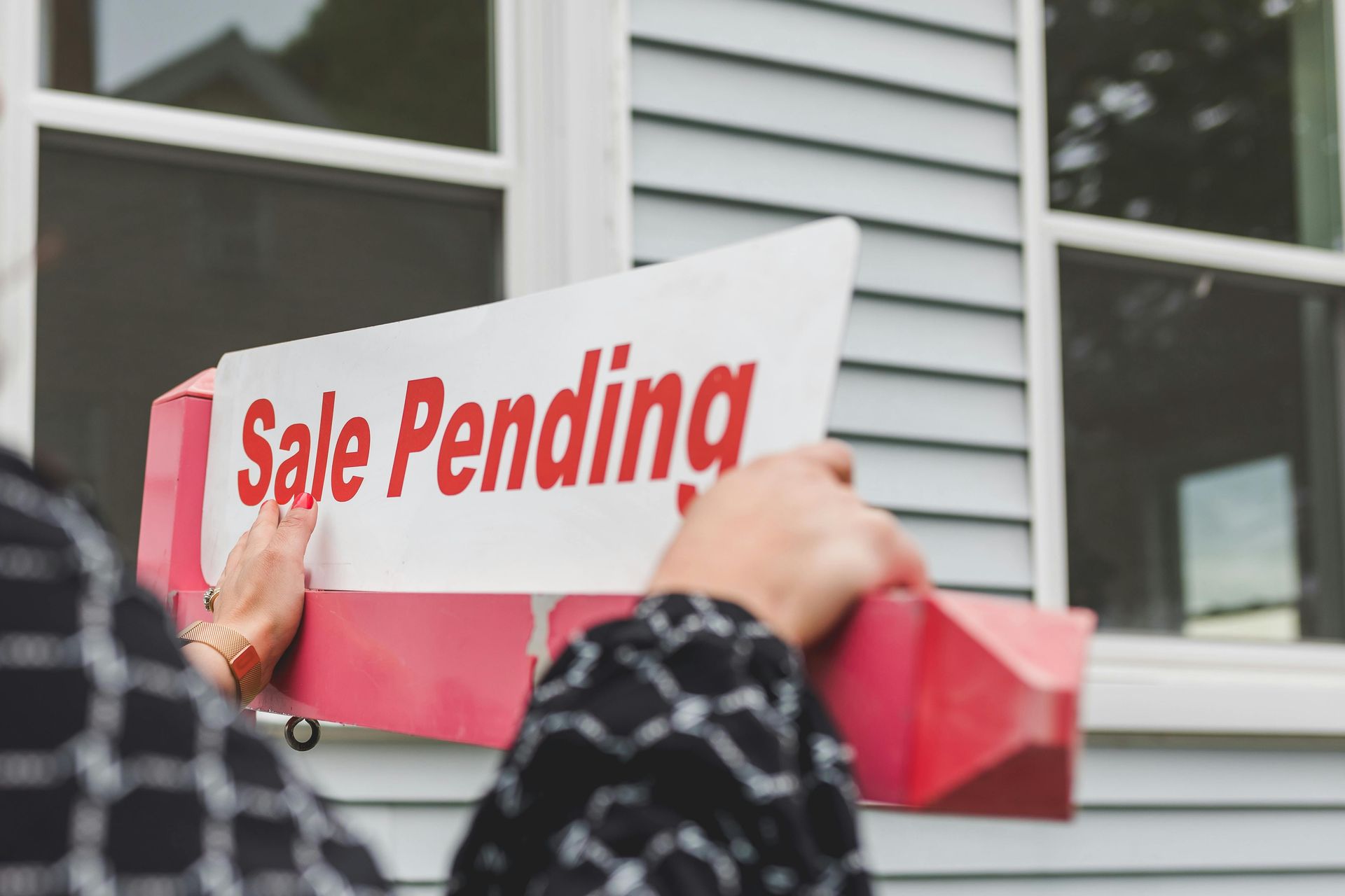 A person is putting a sale pending sign on the side of a house.
