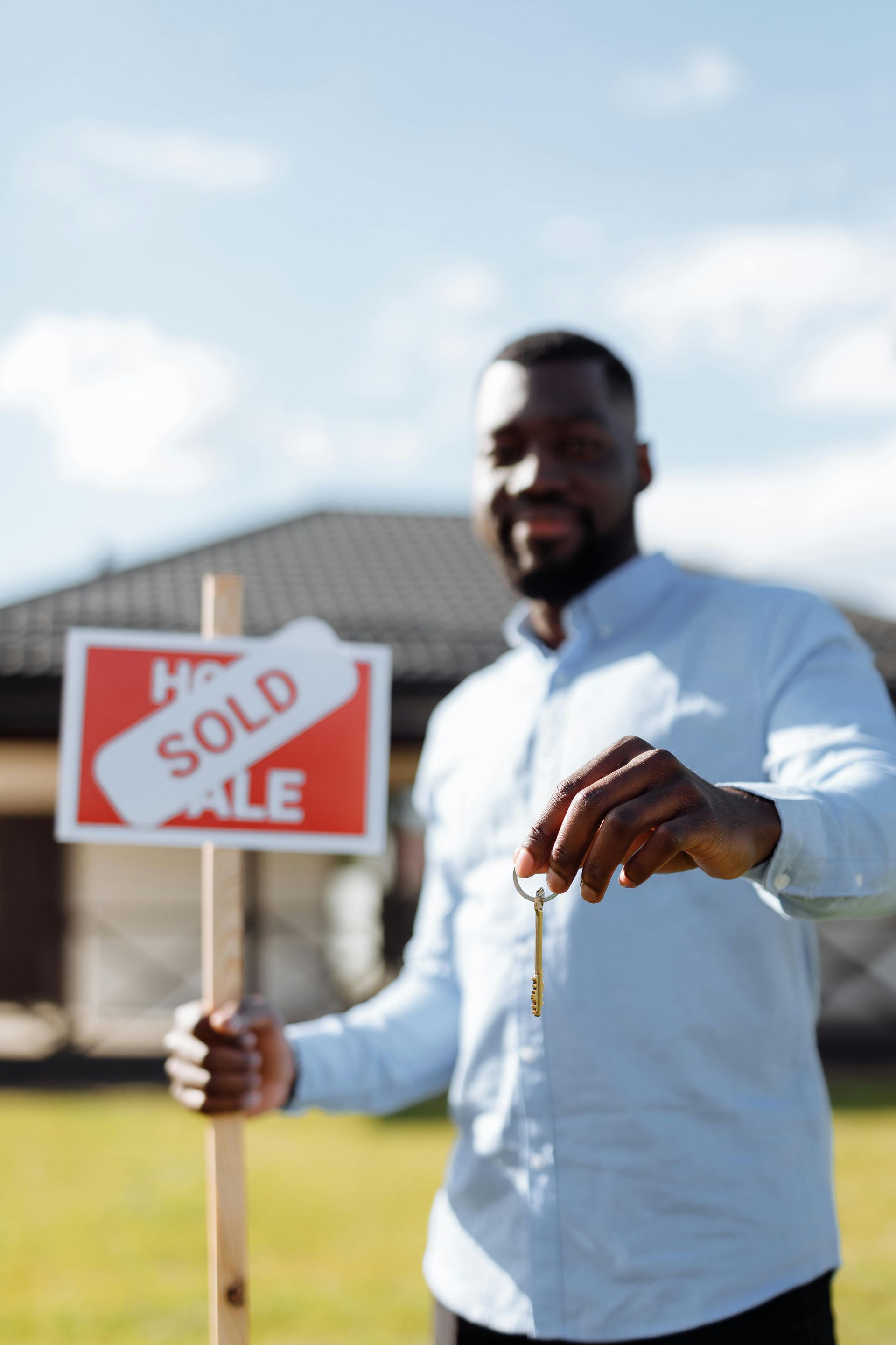 A man is holding a sold sign and keys in front of a house.