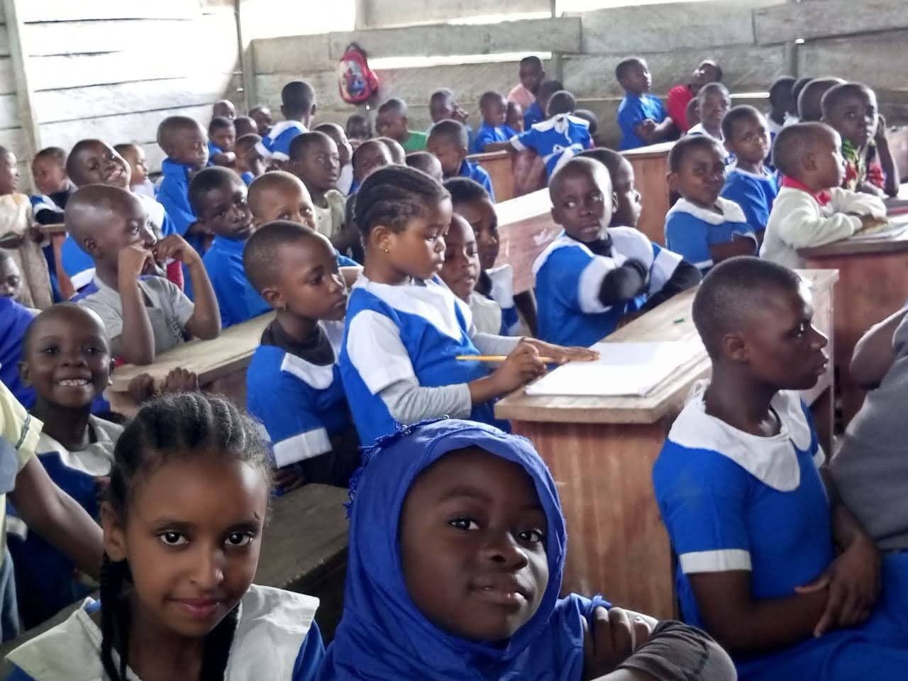 Students in blue-and-white uniforms seated in a crowded classroom, facing forward