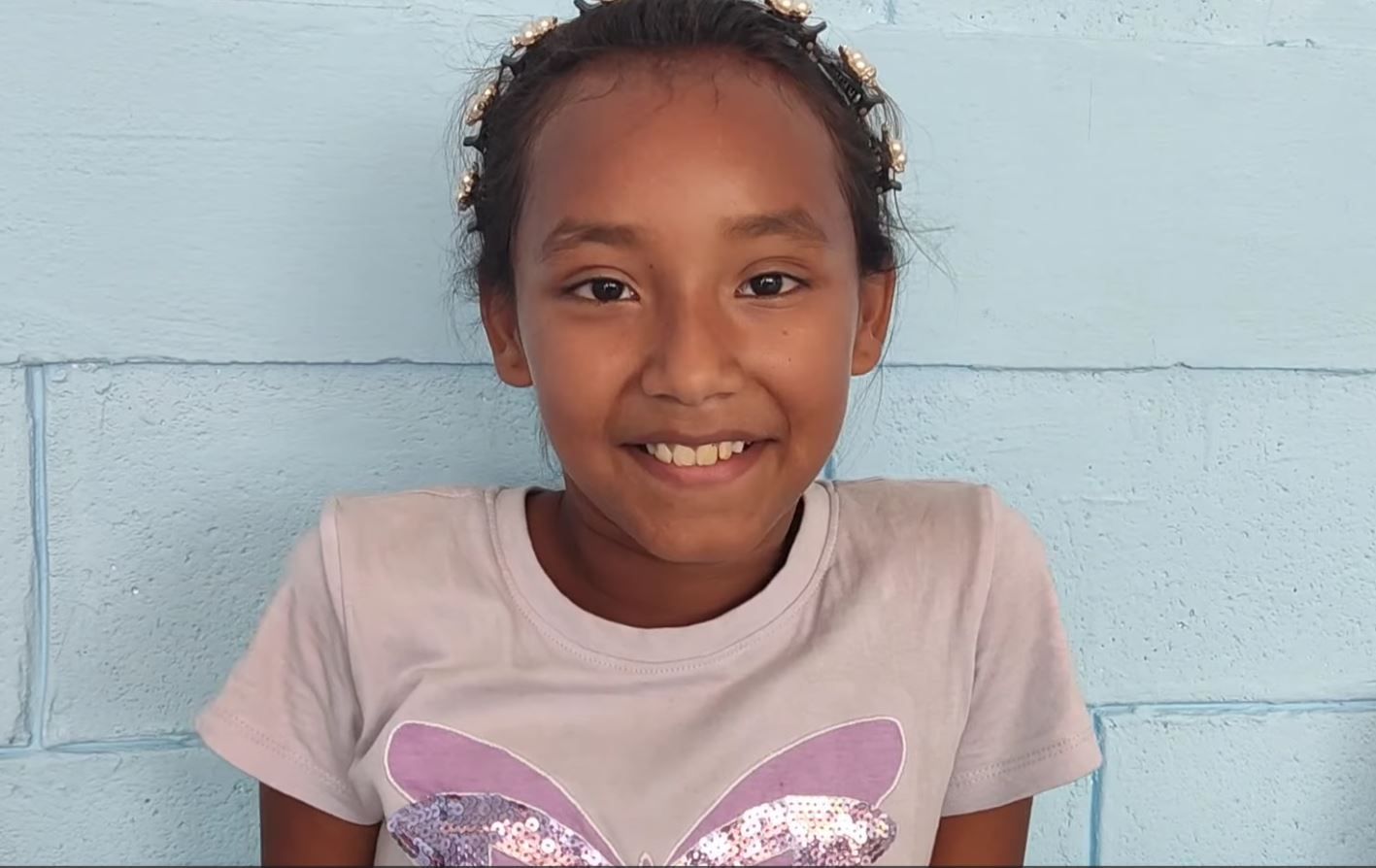 Smiling child in a light pink shirt with a glitter butterfly design against a blue wall