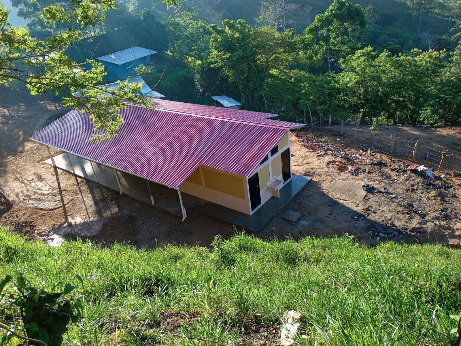 Small house with a red roof on a hillside, surrounded by green trees and brush.