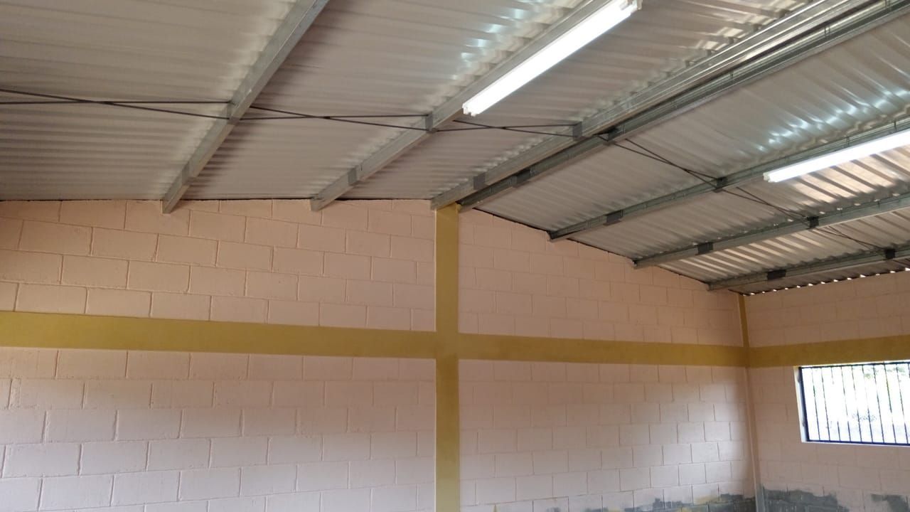 Interior of a warehouse with white brick walls, yellow beams, and a corrugated metal roof.