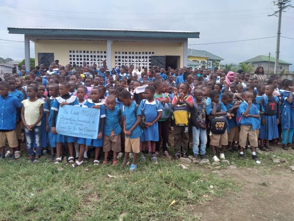 Large group of schoolchildren in blue uniforms gathered outside a building, holding a sign