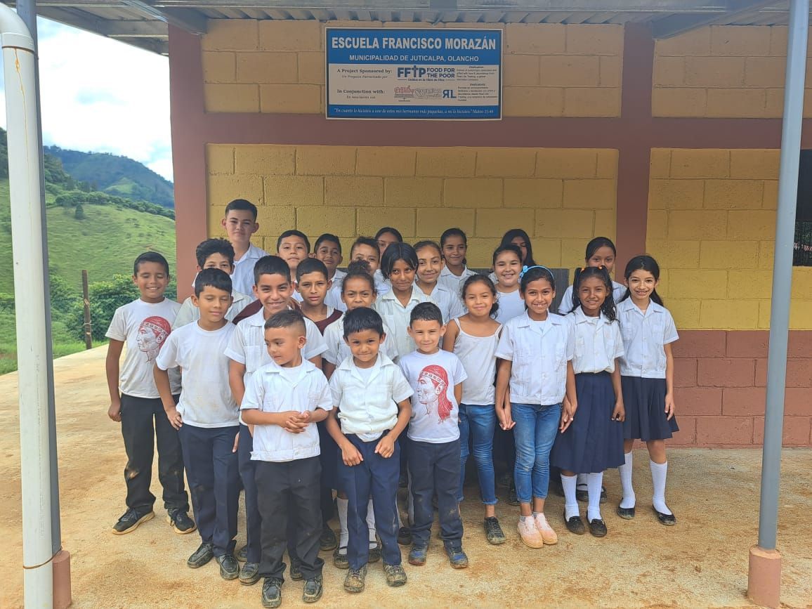 Group of schoolchildren in uniform posing outside a school building under a signboard.