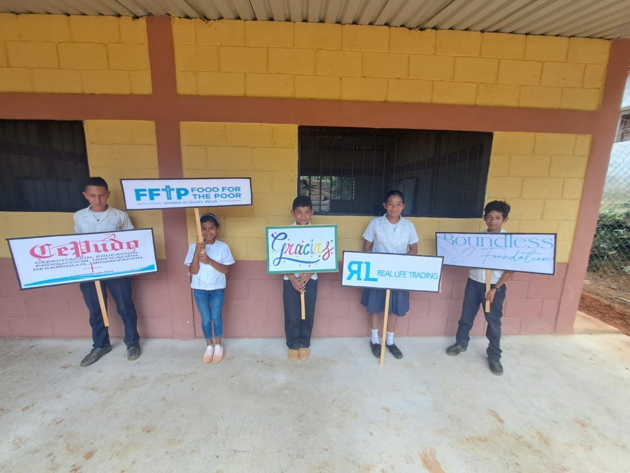 Five people stand outside a yellow building holding signs and banners in a line.