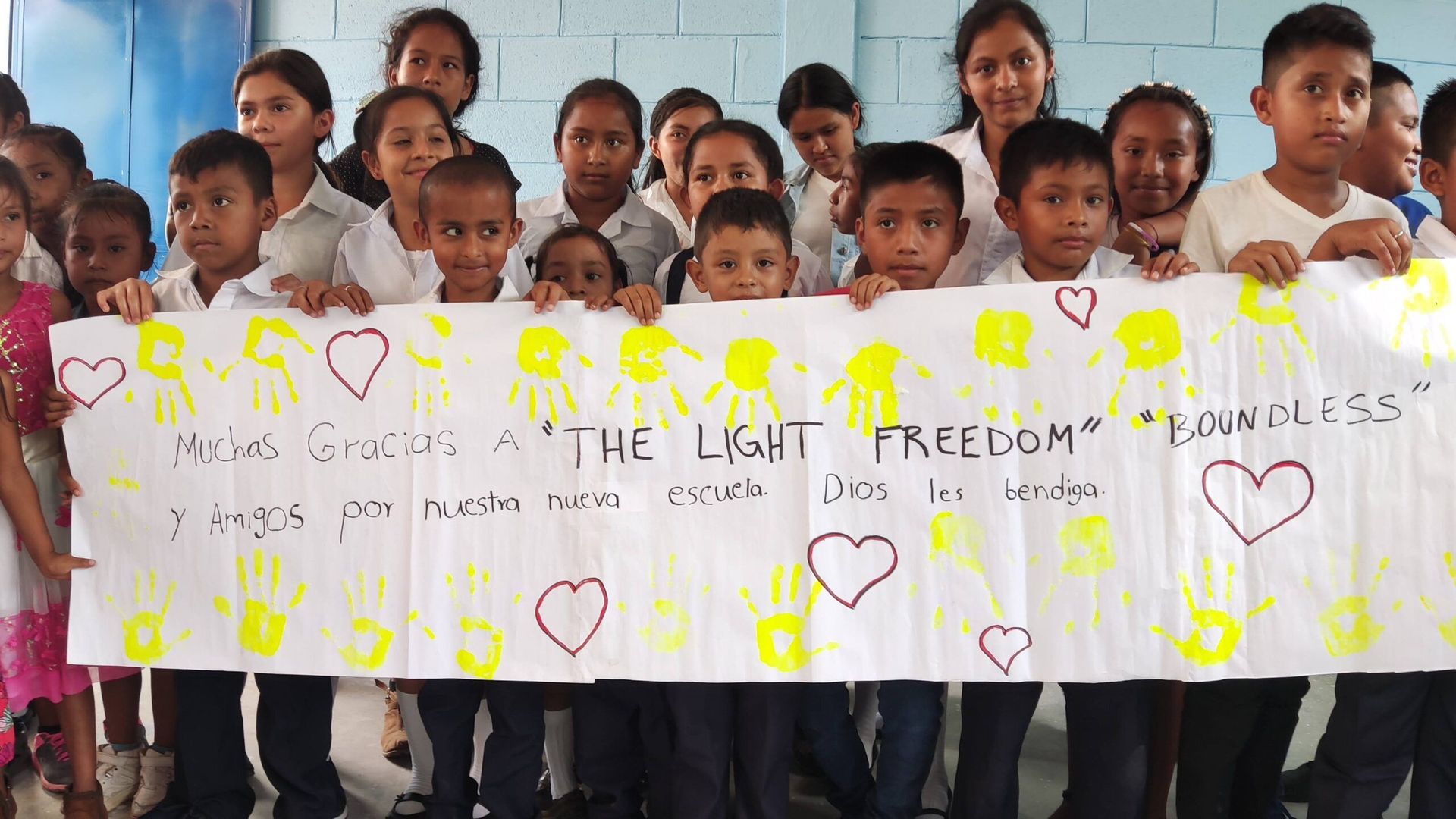 Children holding a banner with handwritten messages and heart drawings in a classroom setting