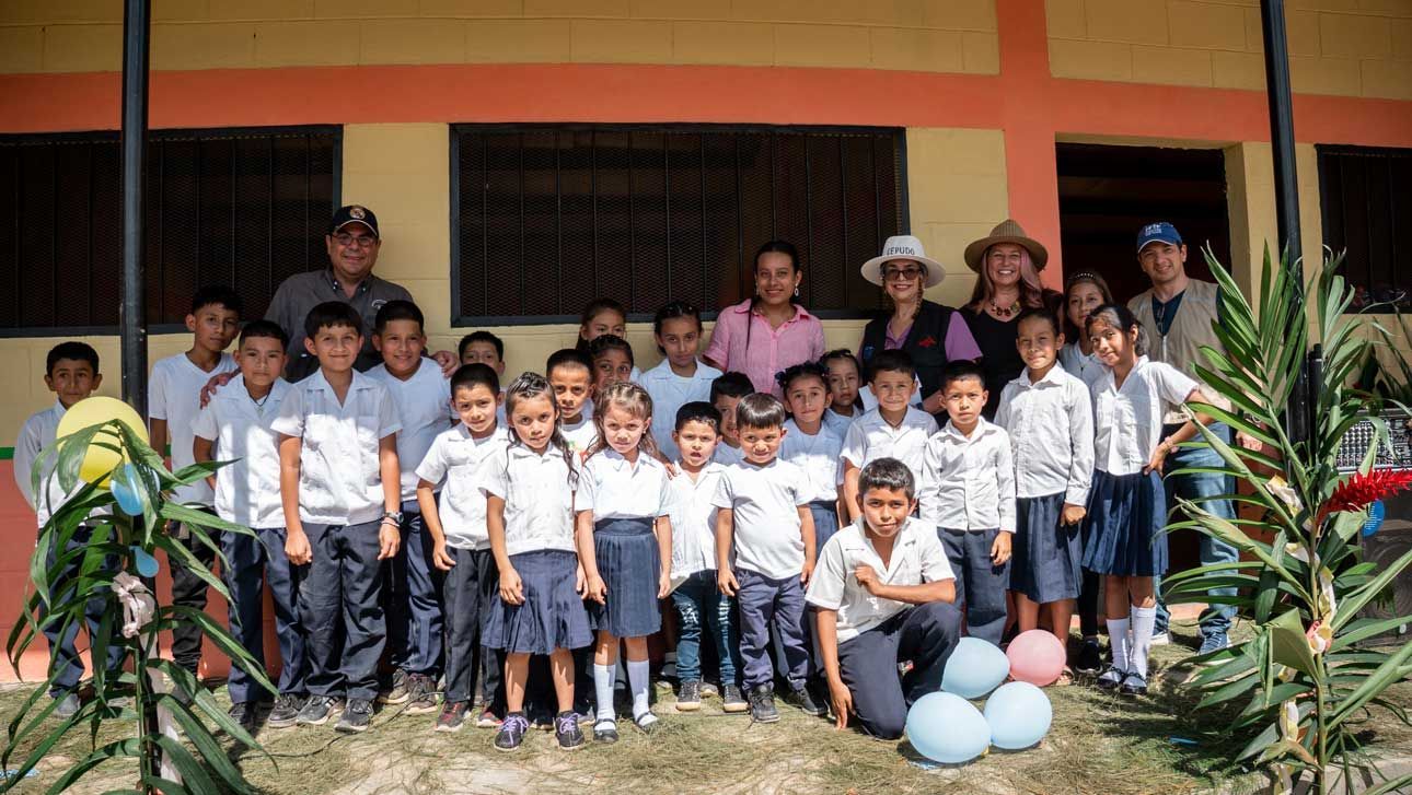 Group of schoolchildren and teachers posing outside a building, with blue balloons in front