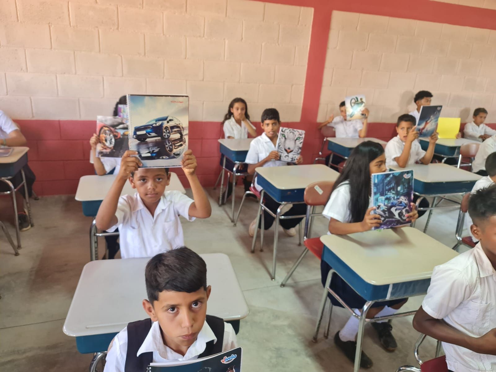 Students seated at desks holding up notebooks in a classroom