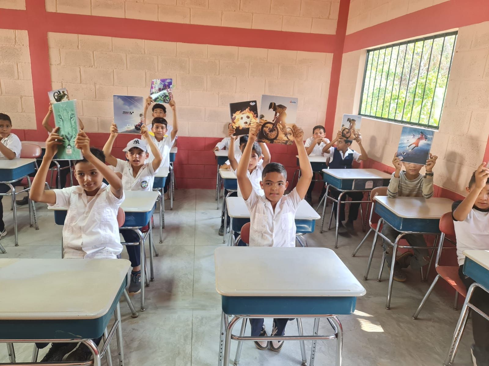 Students in a classroom raising books and hands at their desks