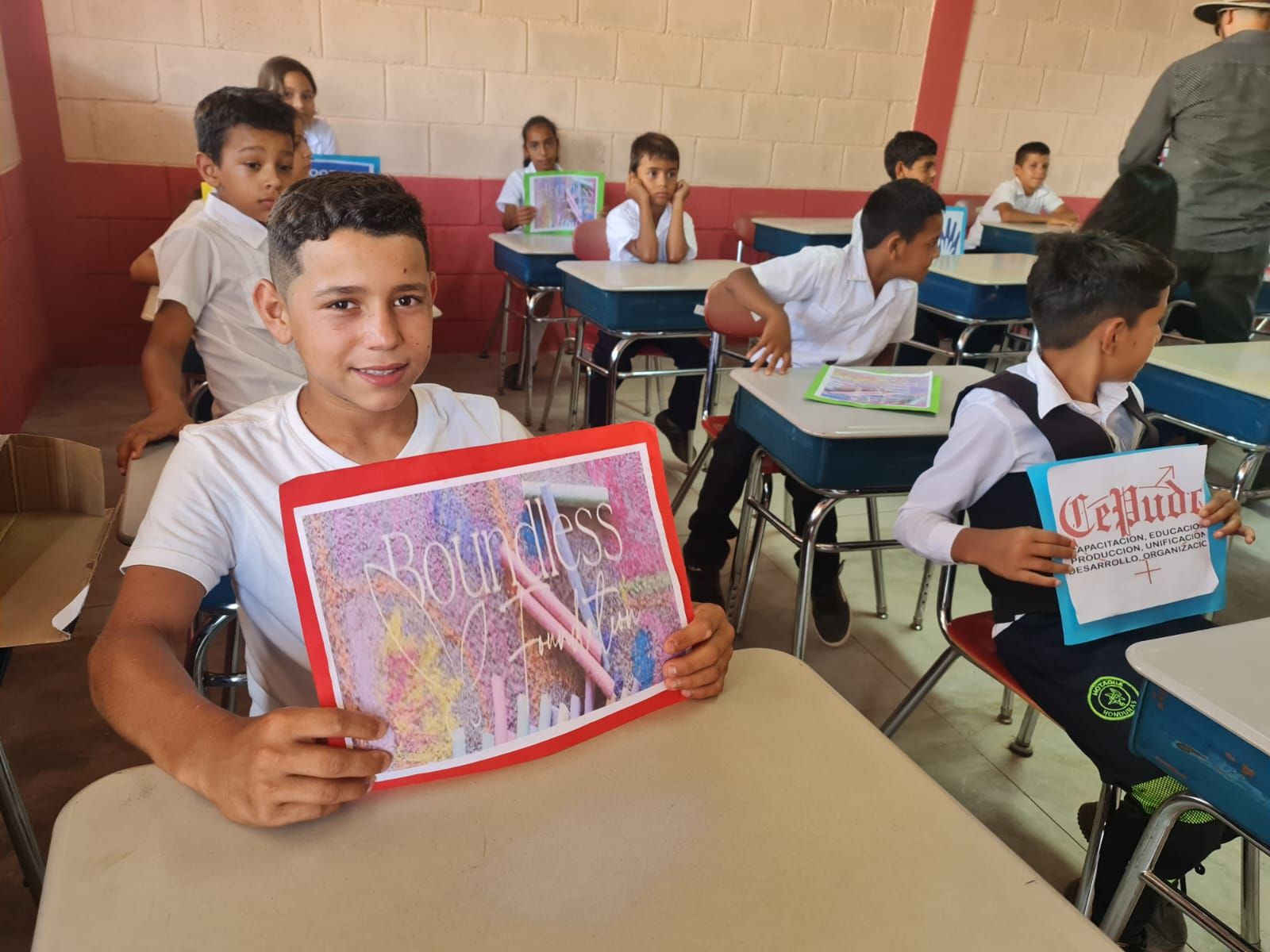 Students seated in a classroom, one holding a red notebook and looking at the camera