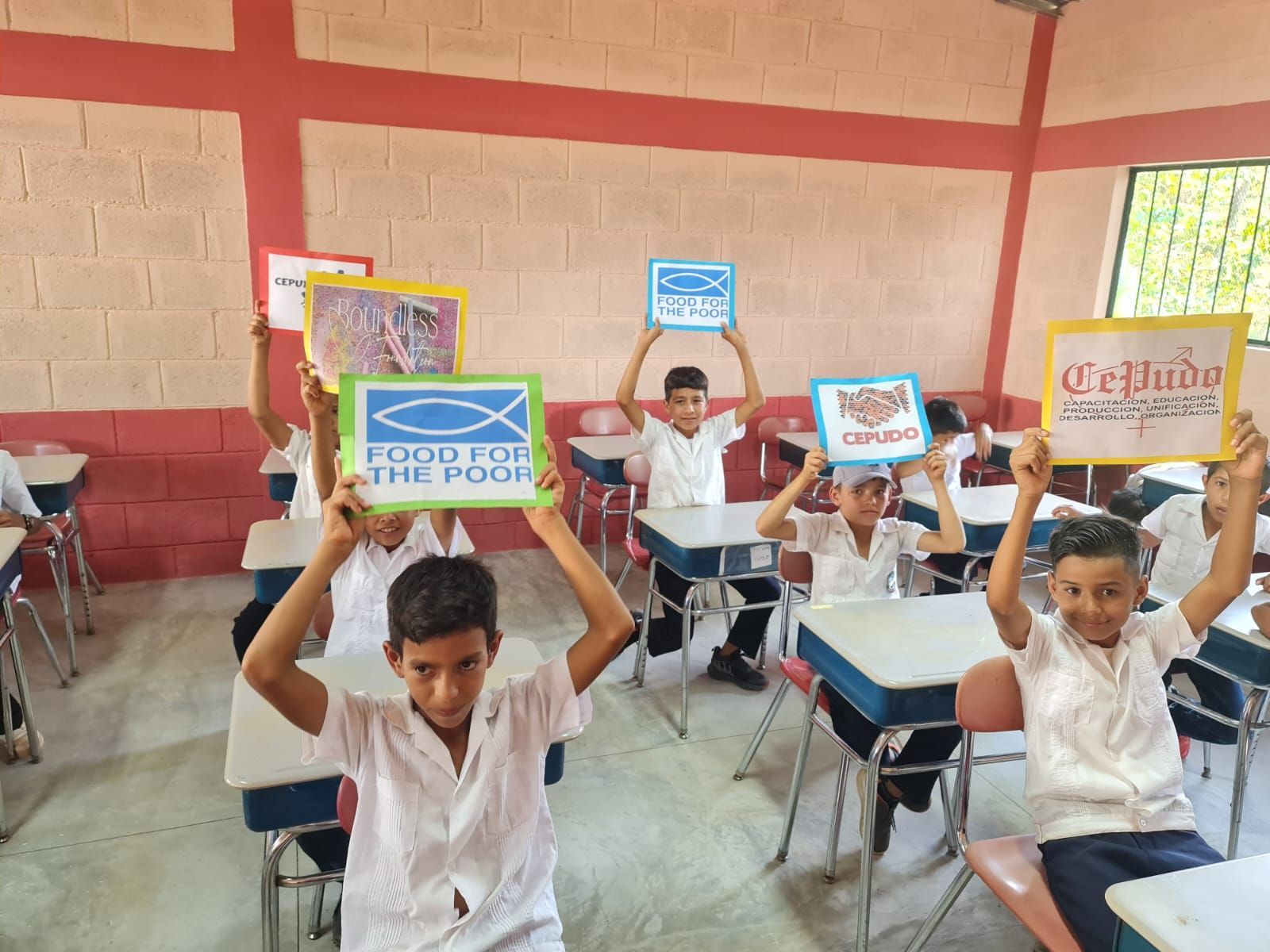 Students in a classroom hold up colorful signs while seated at desks
