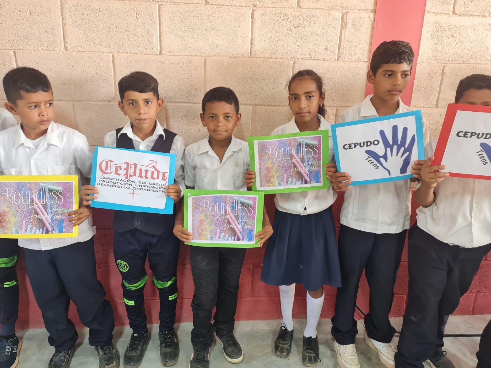 Six students holding colorful notebooks and certificates against a brick wall