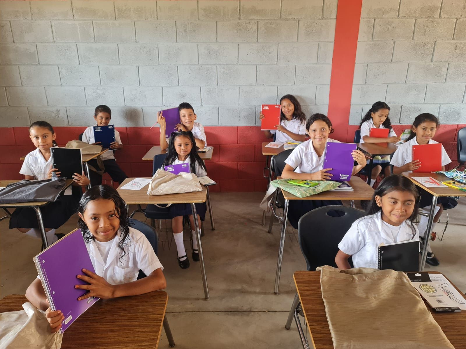 Students seated at desks in a classroom, holding notebooks and tablets.