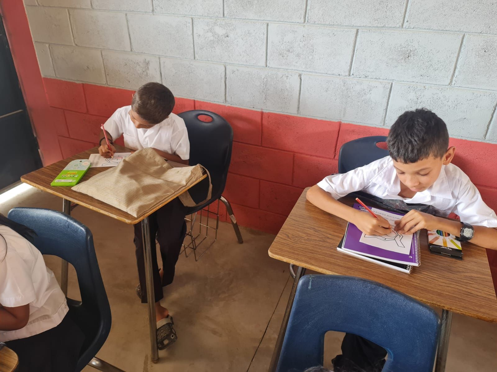 Students writing at desks in a classroom with brick walls and blue chairs
