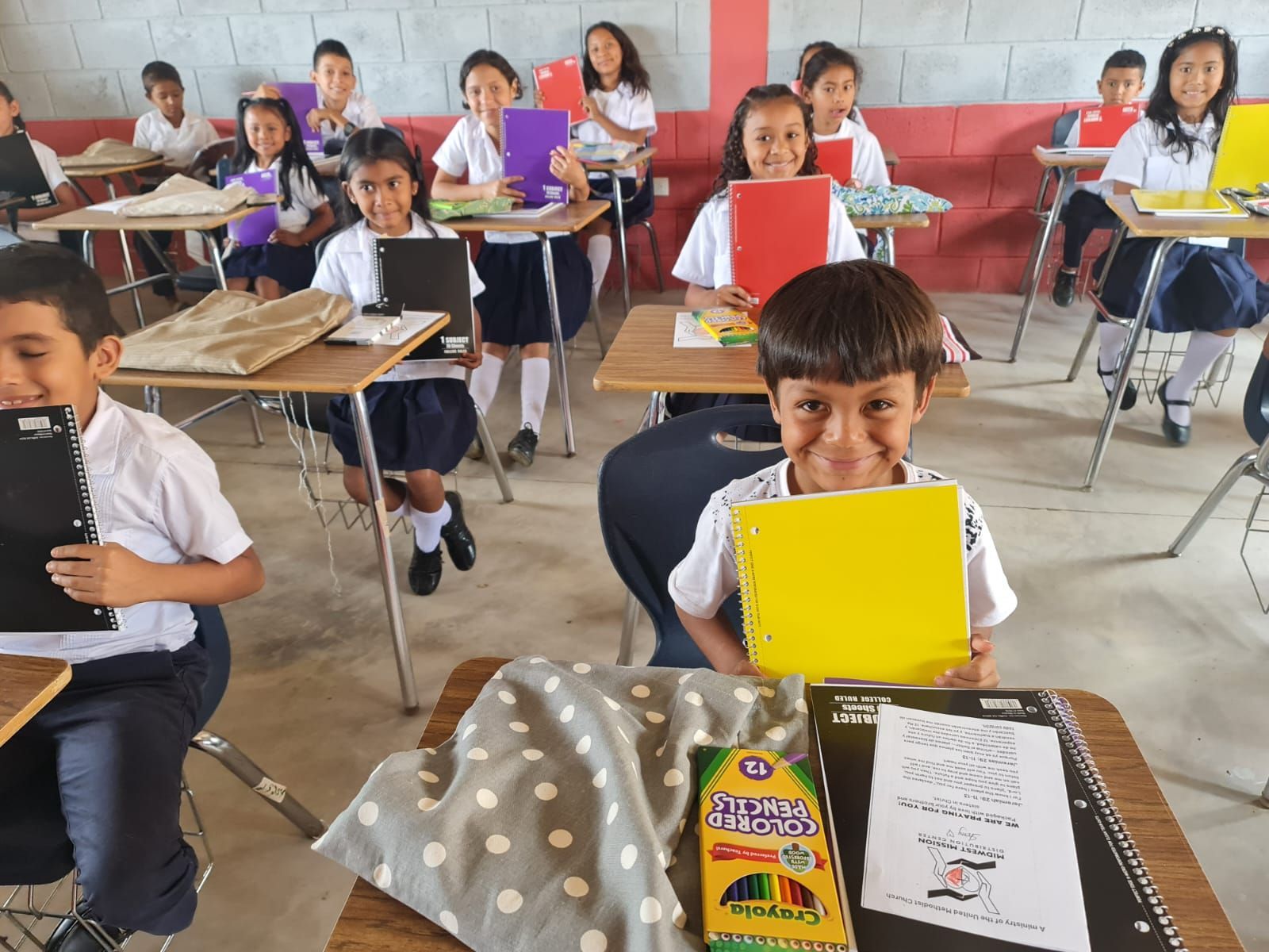 Students seated at desks in a classroom, holding colorful papers during an activity.