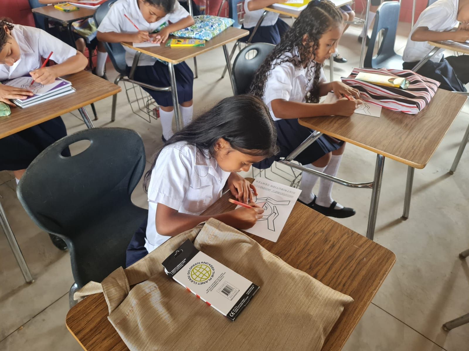 Students working quietly at desks in a classroom, writing in notebooks and reading worksheets.