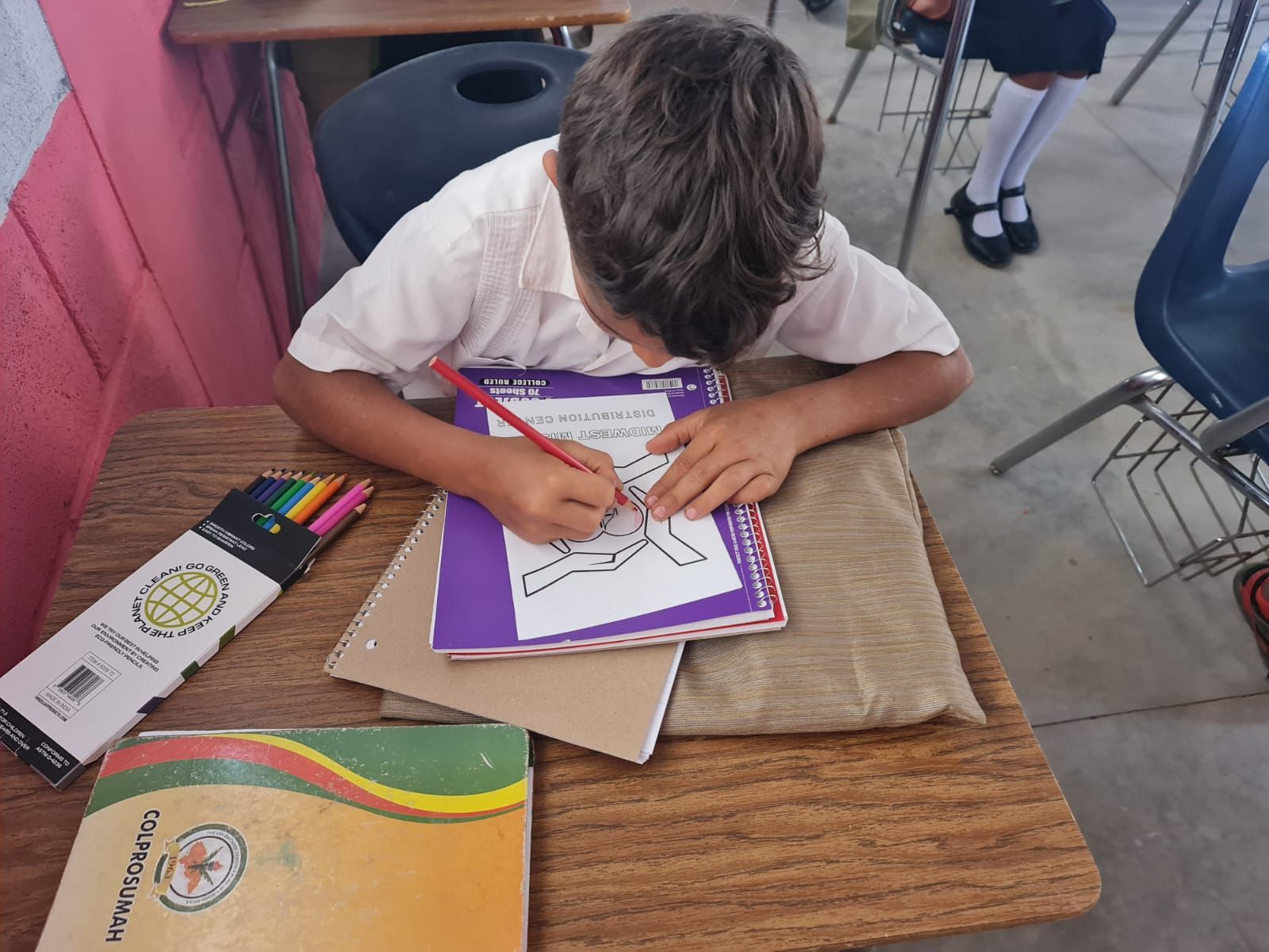 Student drawing with colored pencils at a desk in a classroom.