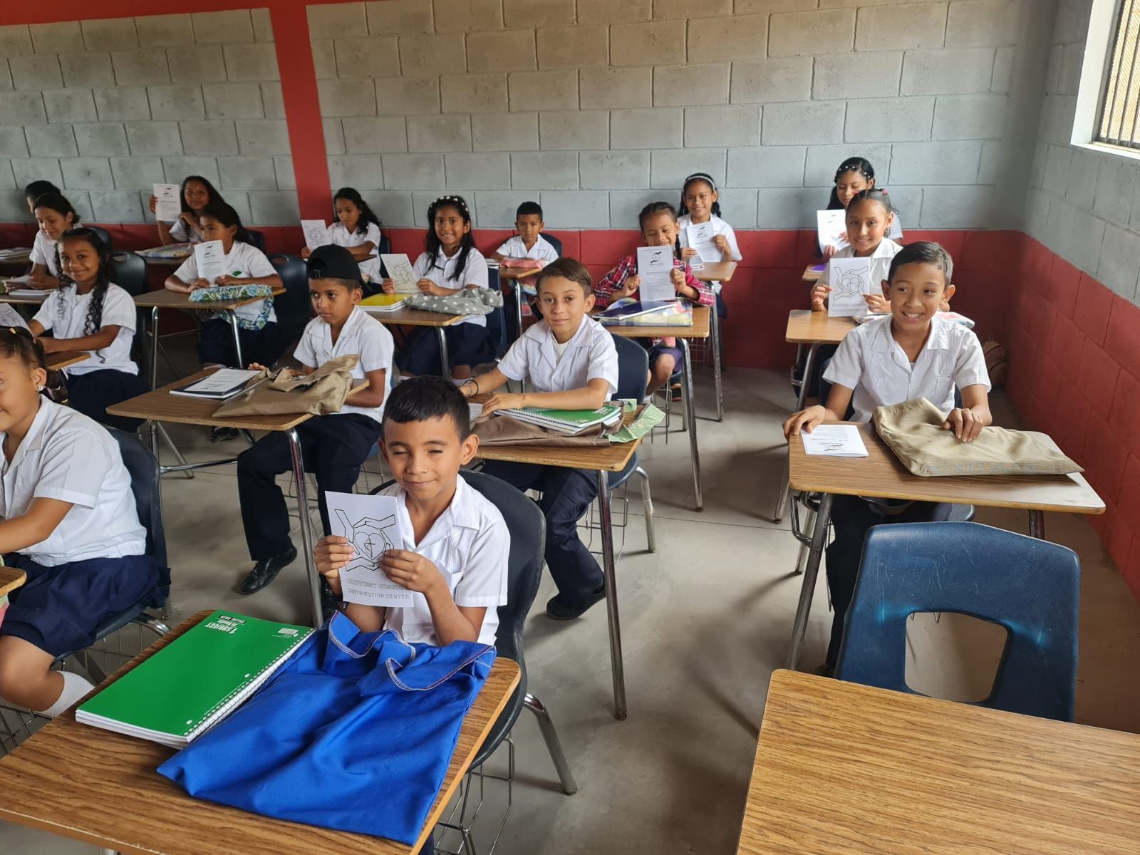 Classroom of students seated at desks, facing forward with notebooks in a simple schoolroom.