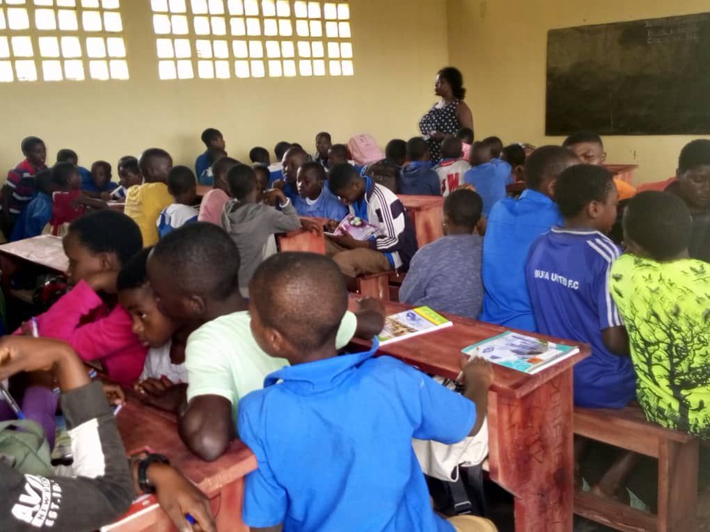 Students seated at wooden desks in a classroom, facing the front during a lesson.
