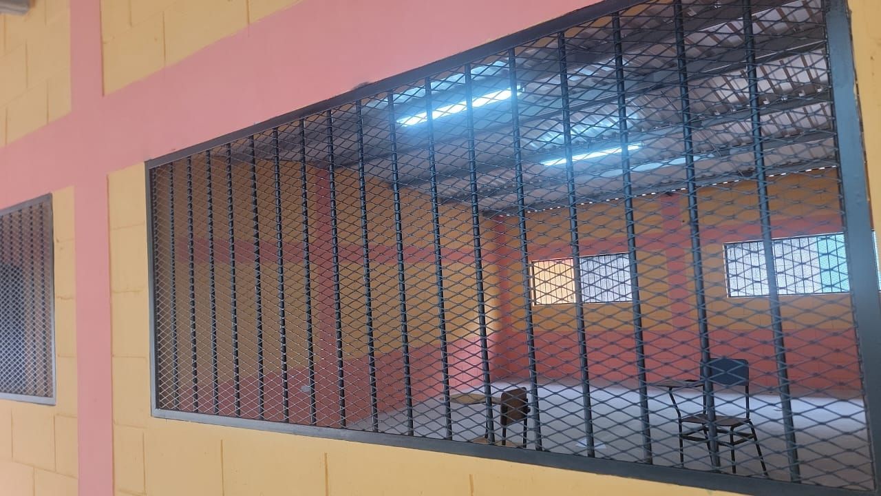 Grilled window in a peach-colored building, looking into an empty room with chairs and bright ceiling lights