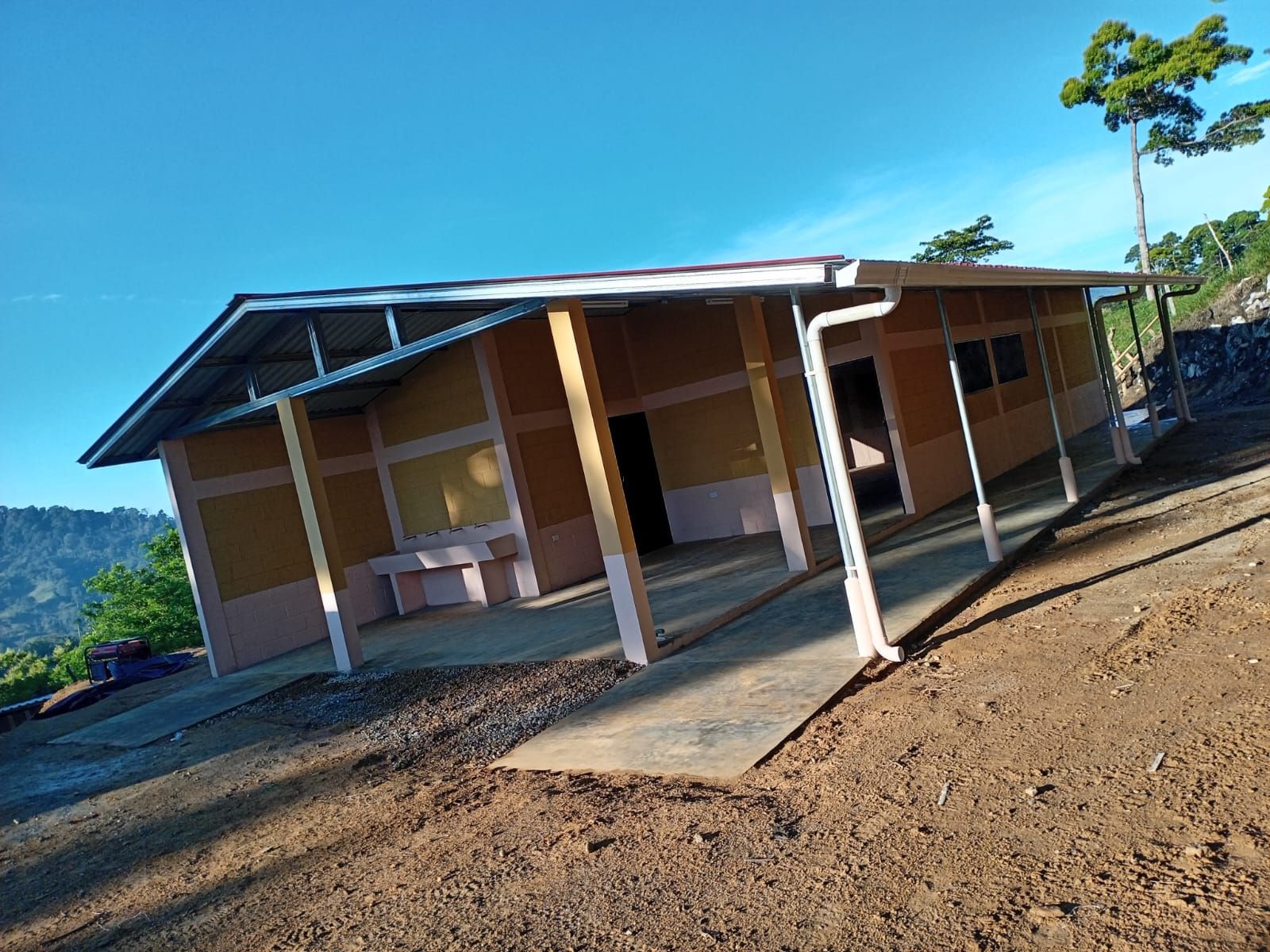 Small rural house with a porch on a sloped dirt lot under a clear blue sky