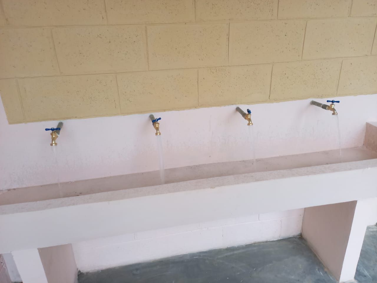 Row of wall-mounted drinking fountains above a concrete basin in a tiled outdoor wash area