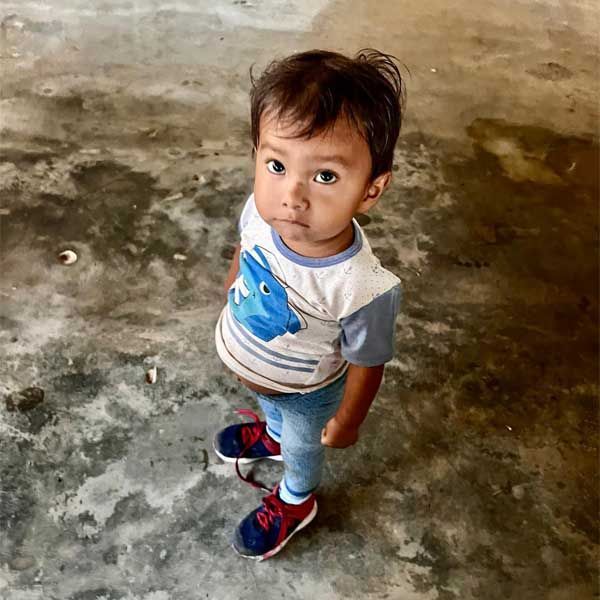Young child standing on a concrete floor, looking up, wearing a white shirt with blue sleeves, jeans, and red sneakers