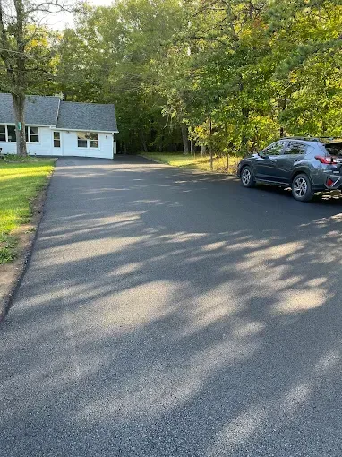 Driveway beside a white house with trees and a parked gray SUV in late afternoon light