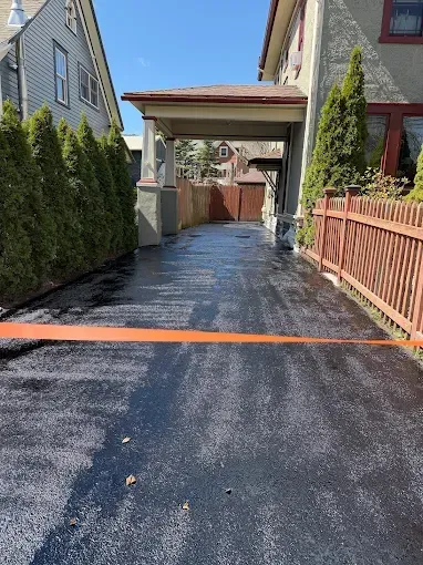 Driveway beside townhouses, with a carport overhead and wet pavement reflecting sunlight.